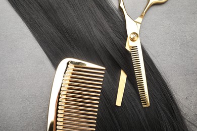 Photo of Black hair strand, comb and professional scissors on grey surface, flat lay