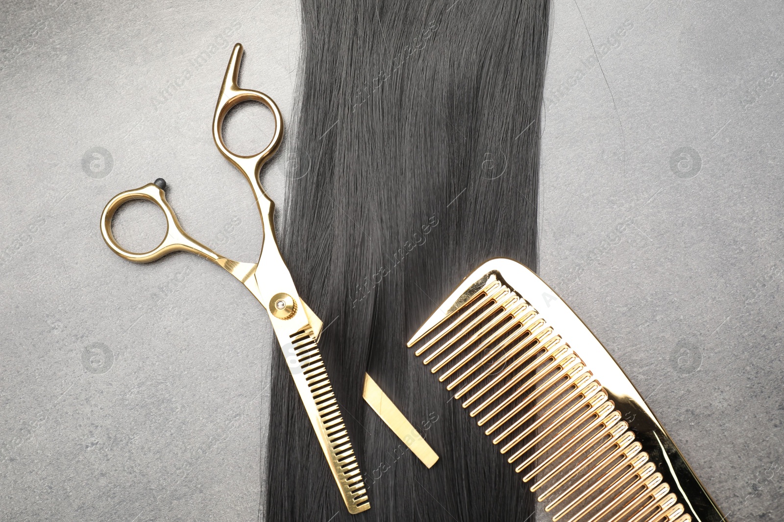 Photo of Black hair strand, comb and professional scissors on grey surface, flat lay