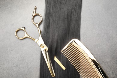 Photo of Black hair strand, comb and professional scissors on grey surface, flat lay