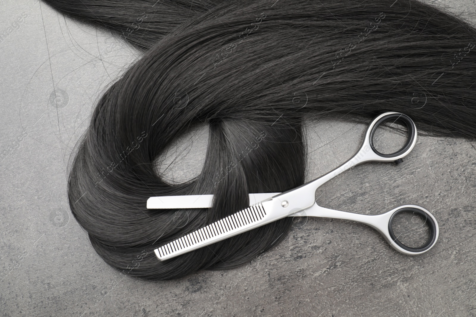 Photo of Black hair strand and professional scissors on grey surface, flat lay