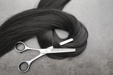 Black hair strand and professional scissors on grey surface, flat lay