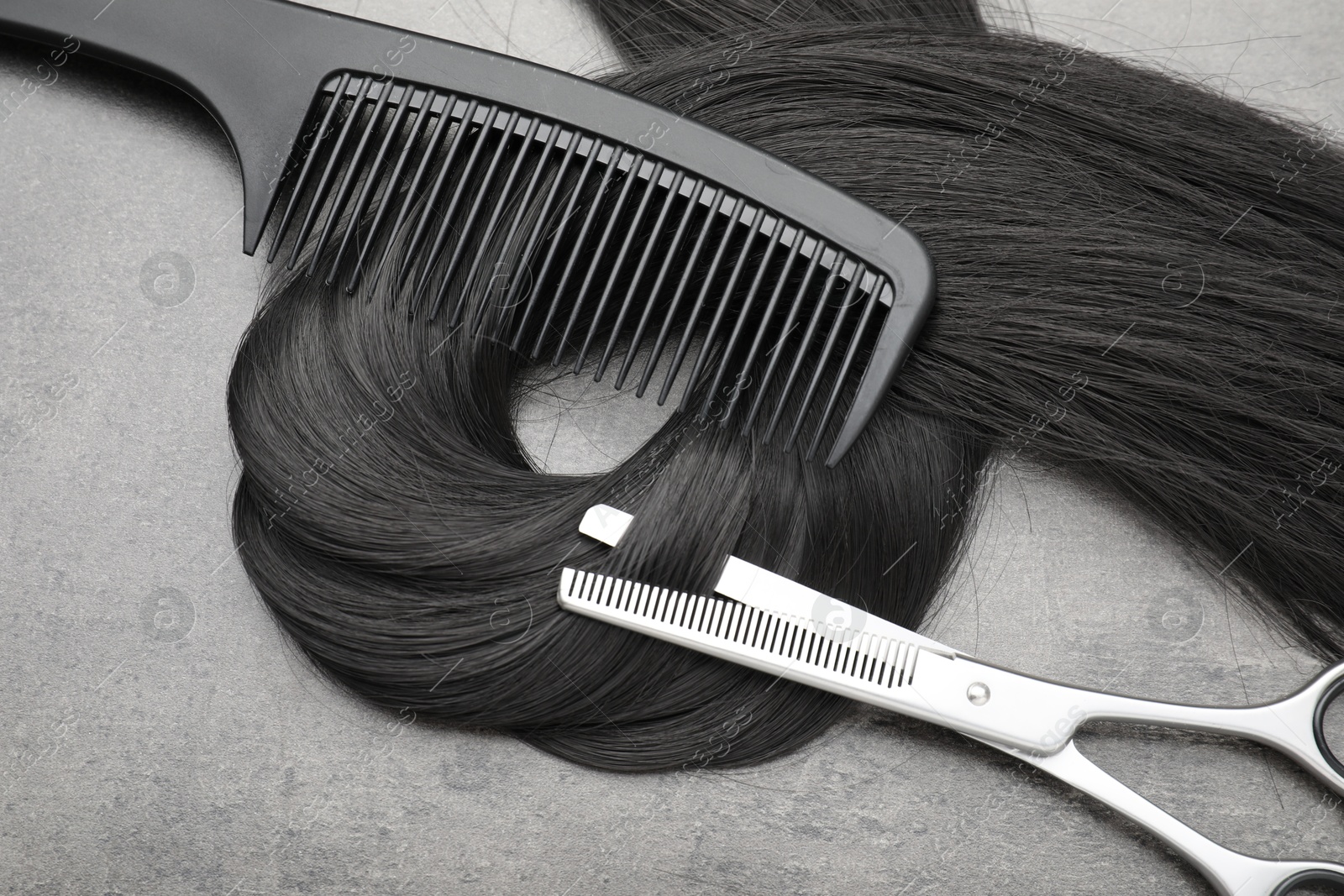 Photo of Black hair strand, comb and professional scissors on grey surface, flat lay