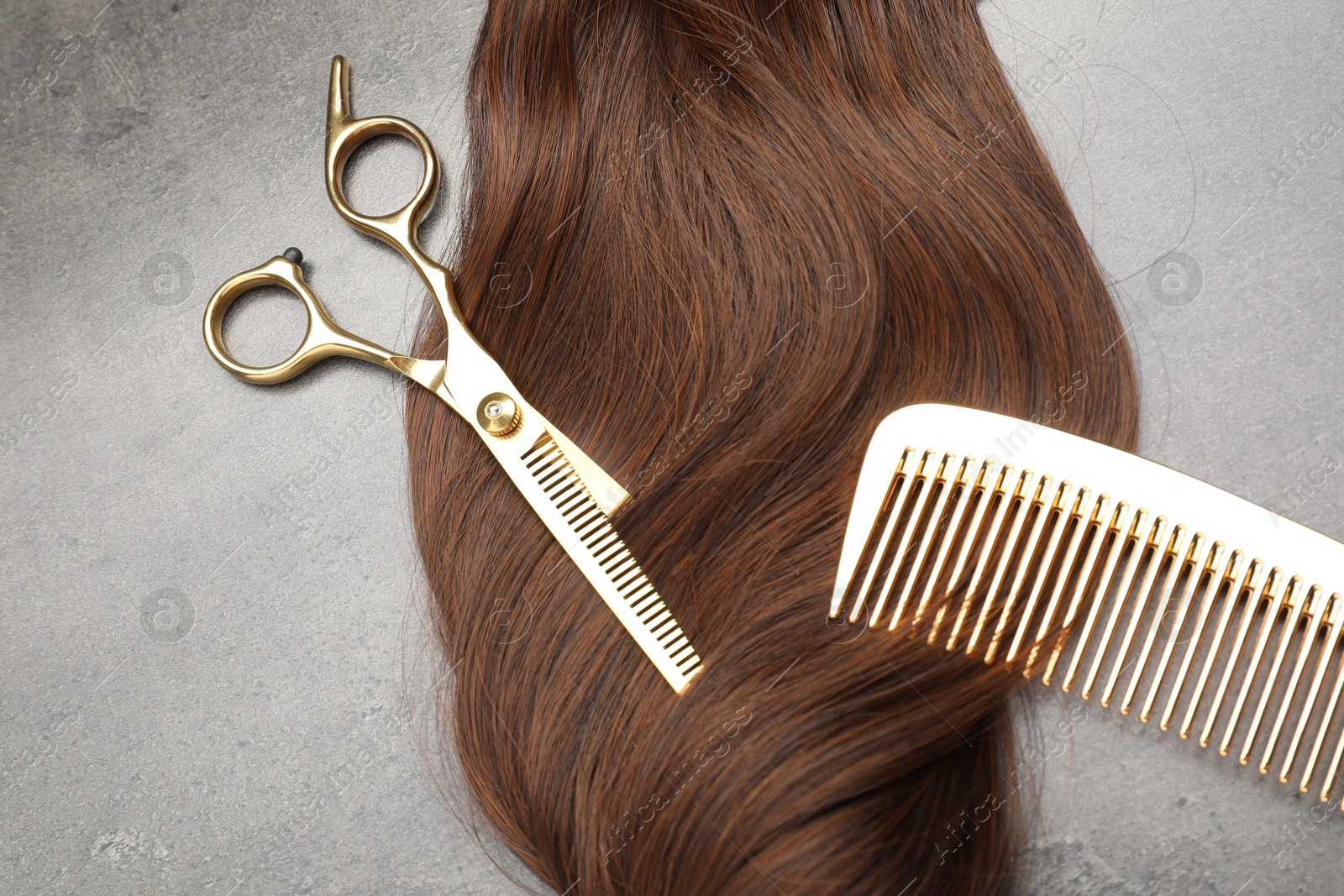 Photo of Brown hair strand, comb and professional scissors on grey surface, flat lay