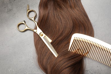 Photo of Brown hair strand, comb and professional scissors on grey surface, flat lay