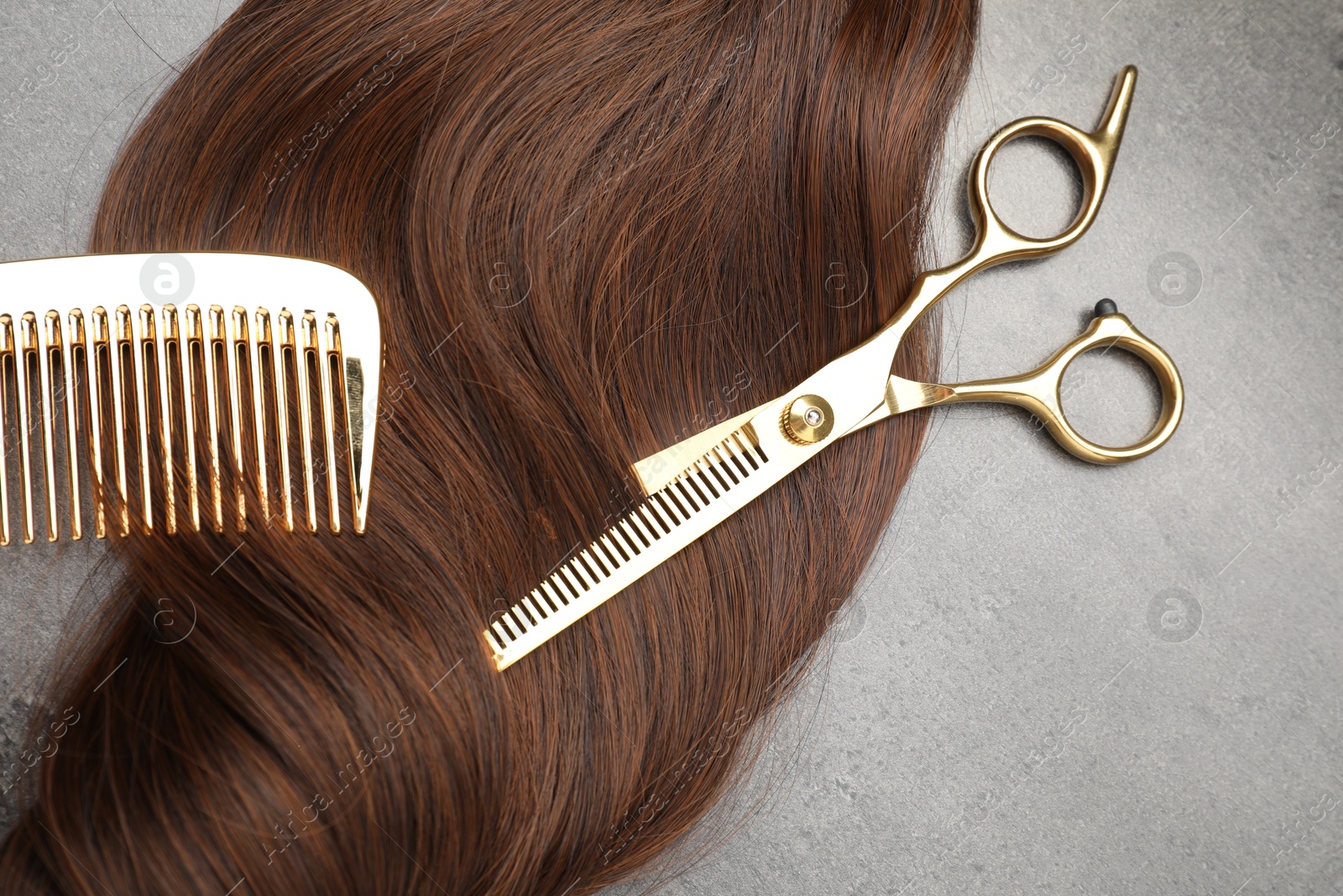 Photo of Brown hair strand, comb and professional scissors on grey surface, flat lay