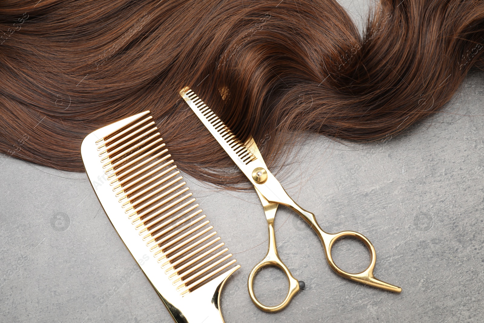 Photo of Brown hair strand, comb and professional scissors on grey surface, flat lay