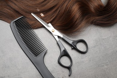 Photo of Brown hair strand, comb and professional scissors on grey surface, flat lay