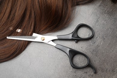 Photo of Brown hair strand and professional scissors on grey surface, flat lay