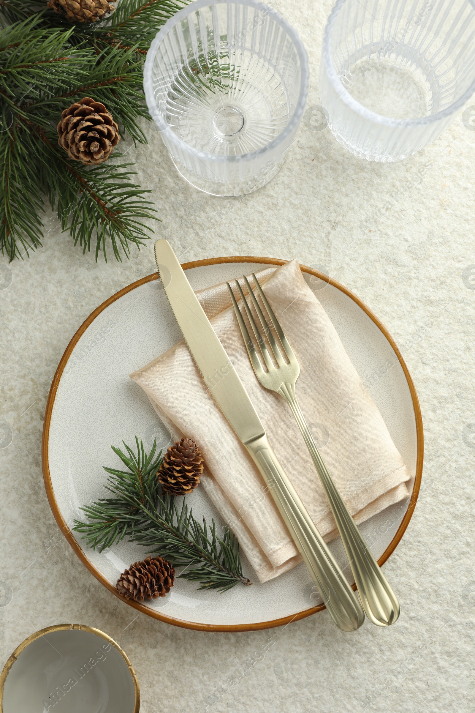 Photo of Christmas table setting with plate, glasses, cutlery, fir branches and cones, flat lay