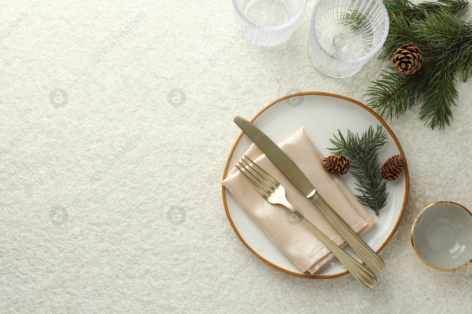 Photo of Christmas table setting with plate, glasses, cutlery, fir branches and cones, flat lay. Space for text