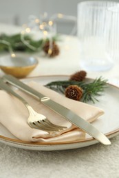 Photo of Christmas table setting with plate, cutlery, fir branches and cones, closeup