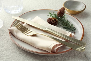 Photo of Christmas table setting with plate, bowl, cutlery, fir branches and cones, closeup