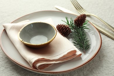 Photo of Christmas table setting with plate, bowl, cutlery, fir branches and cones, closeup