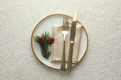 Photo of Christmas table setting with plate, cutlery, fir branch and cones, top view