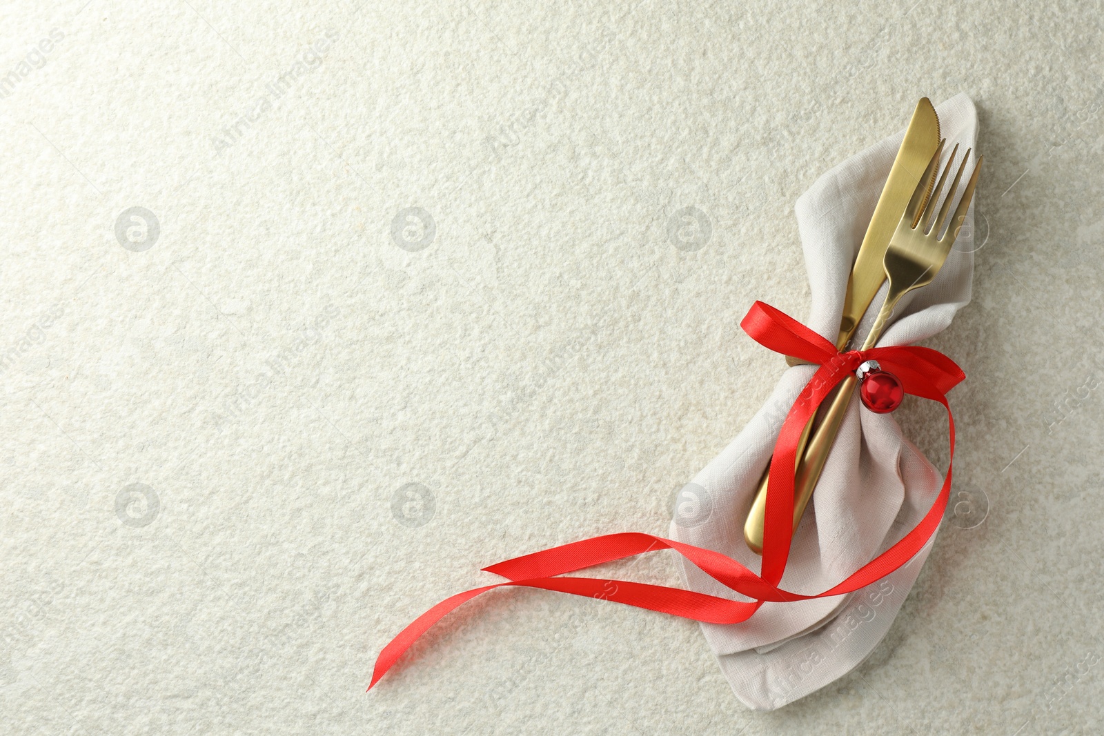 Photo of Christmas table setting. Cutlery, napkin, ribbon and bauble on light textured background, top view. Space for text