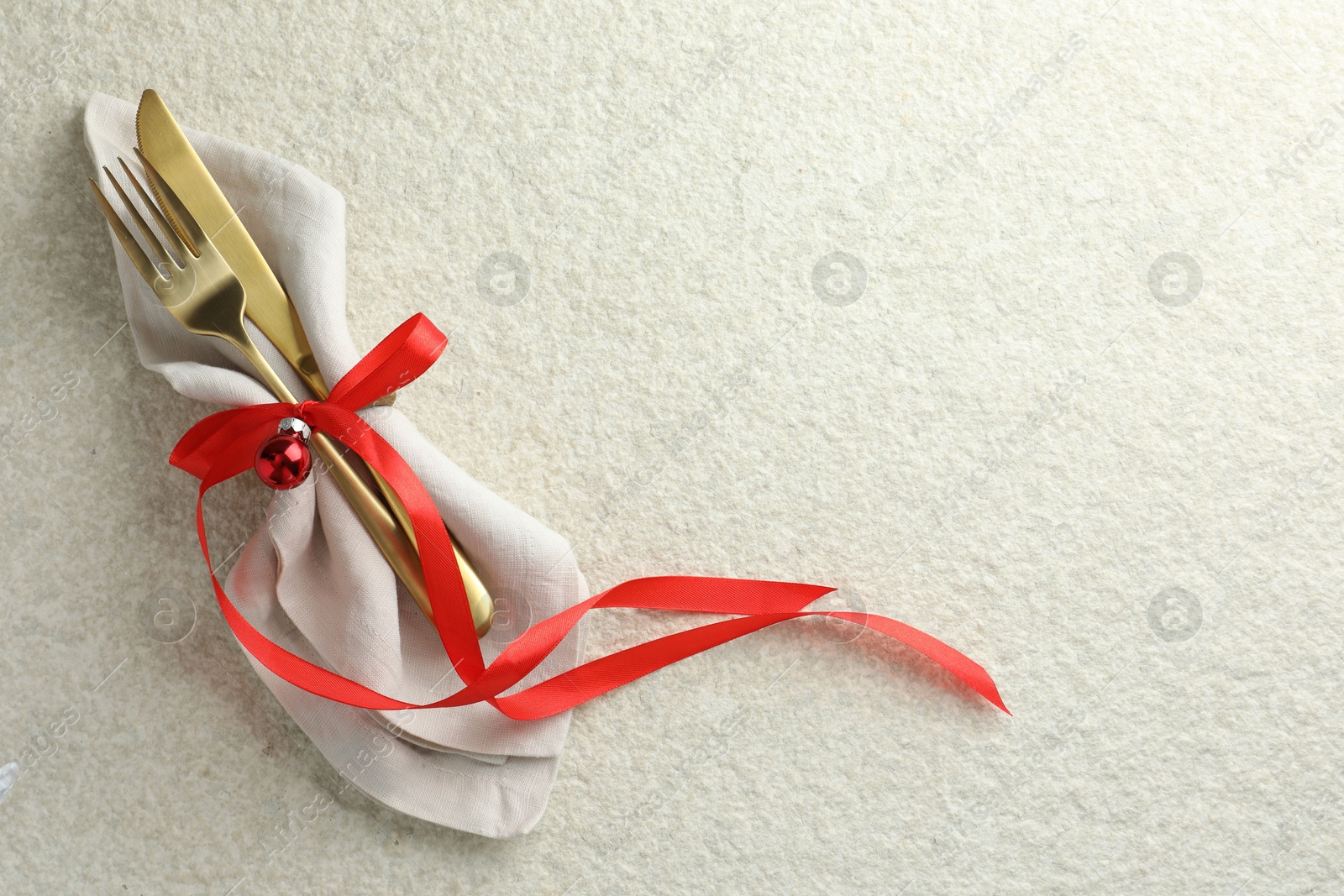 Photo of Christmas table setting. Cutlery, napkin, ribbon and bauble on light textured background, top view. Space for text