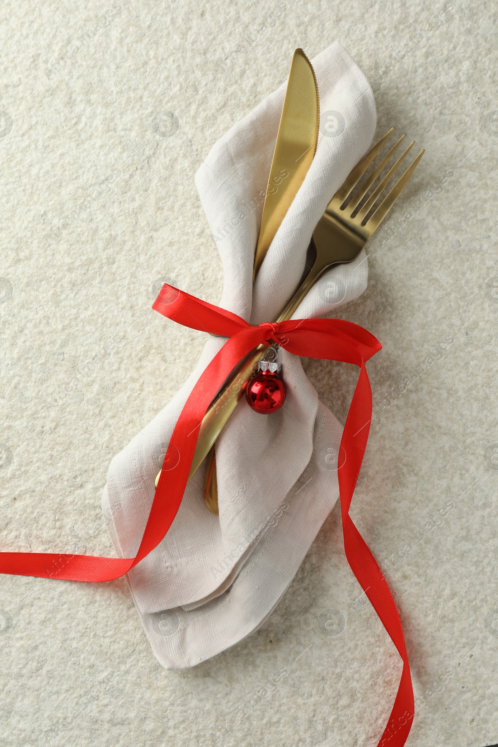 Photo of Christmas table setting. Cutlery, napkin, ribbon and bauble on light textured background, top view