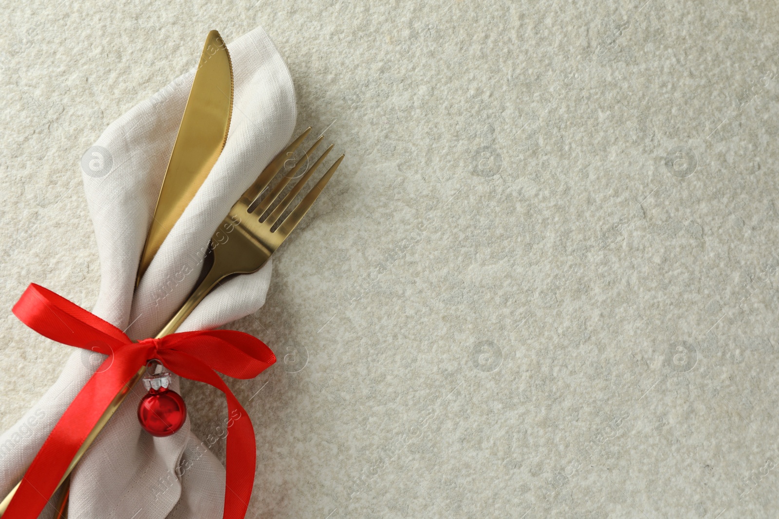 Photo of Christmas table setting. Cutlery, napkin, ribbon and bauble on light textured background, top view. Space for text