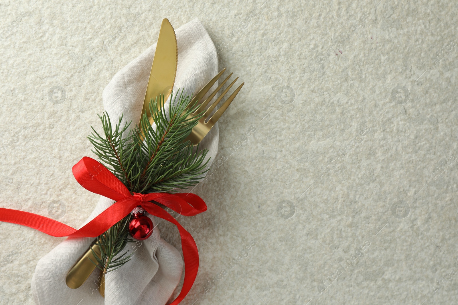 Photo of Christmas table setting. Cutlery, napkin, ribbon, fir branches and bauble on light textured background, top view. Space for text