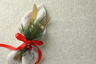 Photo of Christmas table setting. Cutlery, napkin, ribbon, fir branches and bauble on light textured background, top view. Space for text