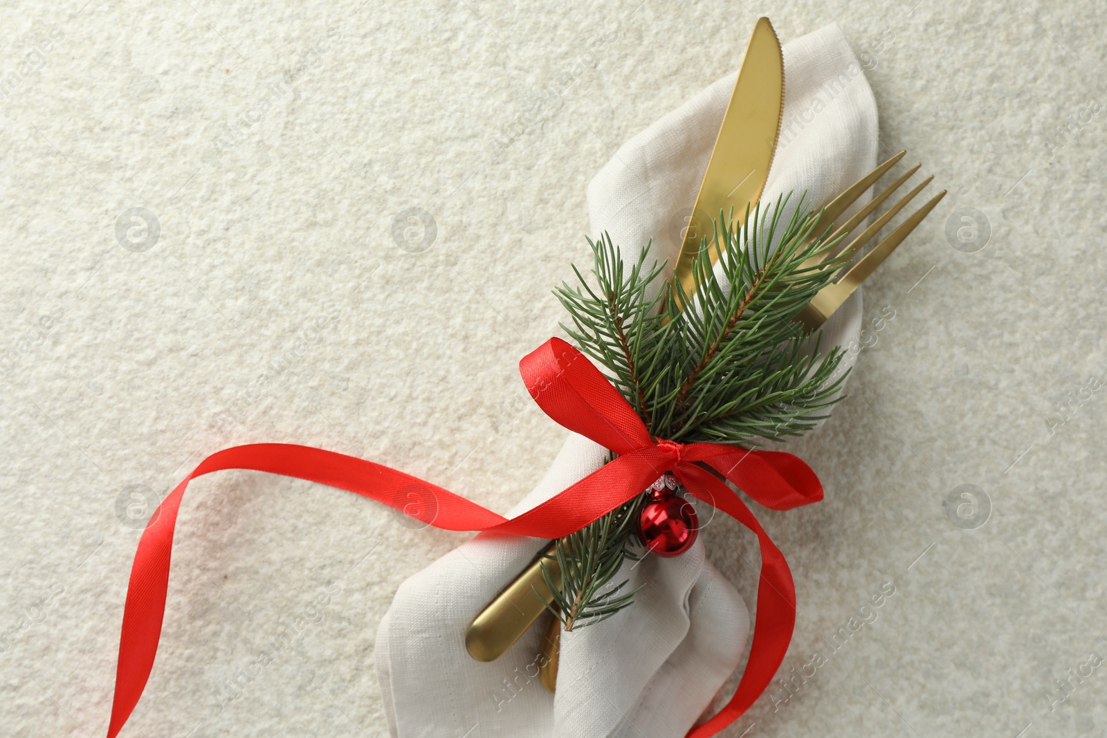 Photo of Christmas table setting. Cutlery, napkin, ribbon, fir branches and bauble on light textured background, top view