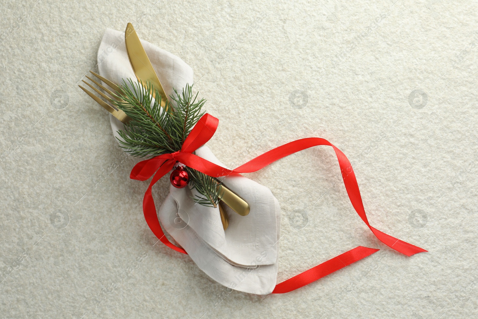 Photo of Christmas table setting. Cutlery, napkin, ribbon, fir branches and bauble on light textured background, top view