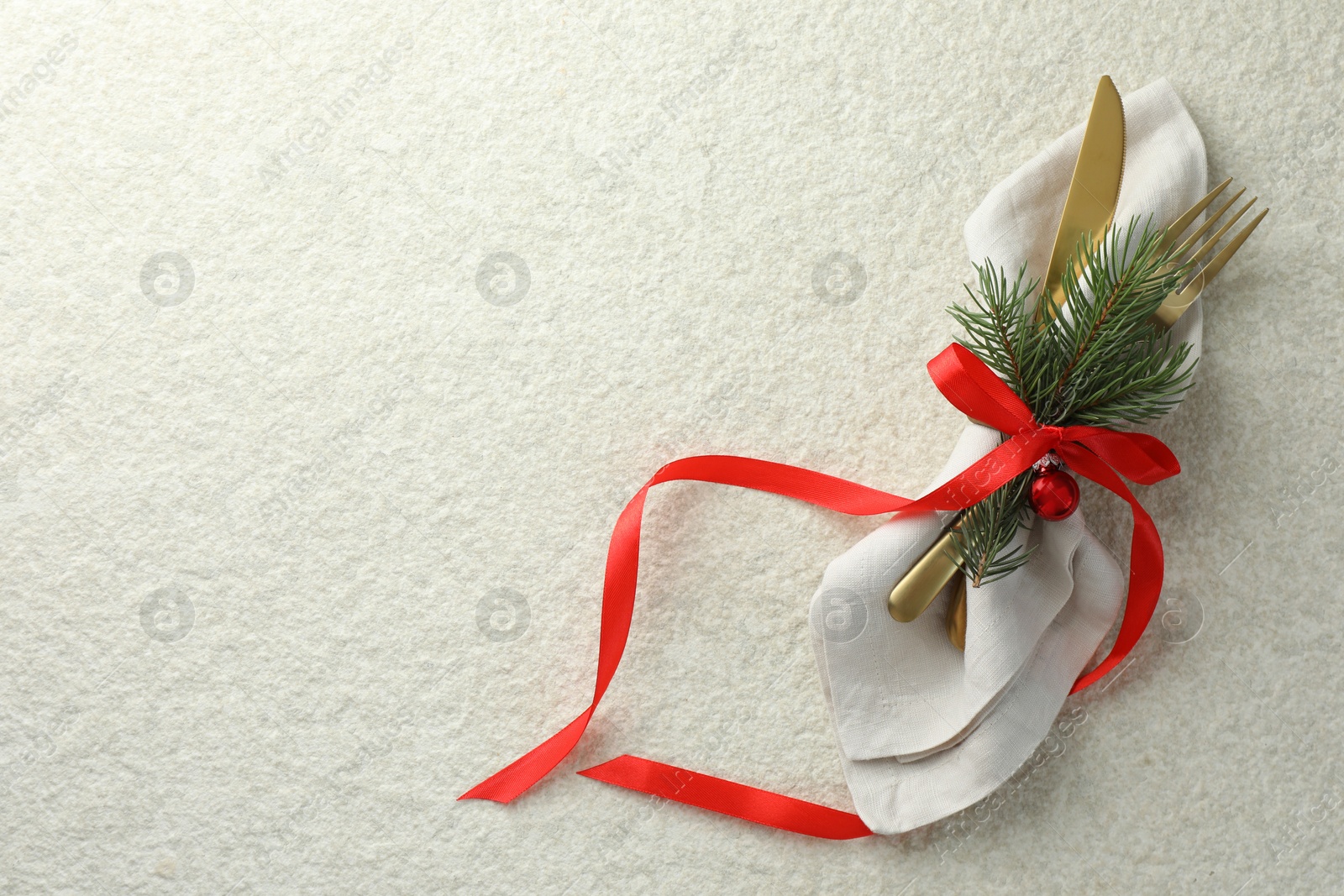 Photo of Christmas table setting. Cutlery, napkin, ribbon, fir branches and bauble on light textured background, top view. Space for text