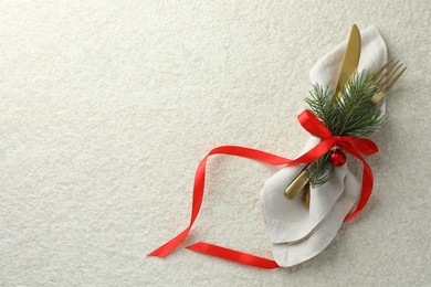 Photo of Christmas table setting. Cutlery, napkin, ribbon, fir branches and bauble on light textured background, top view. Space for text