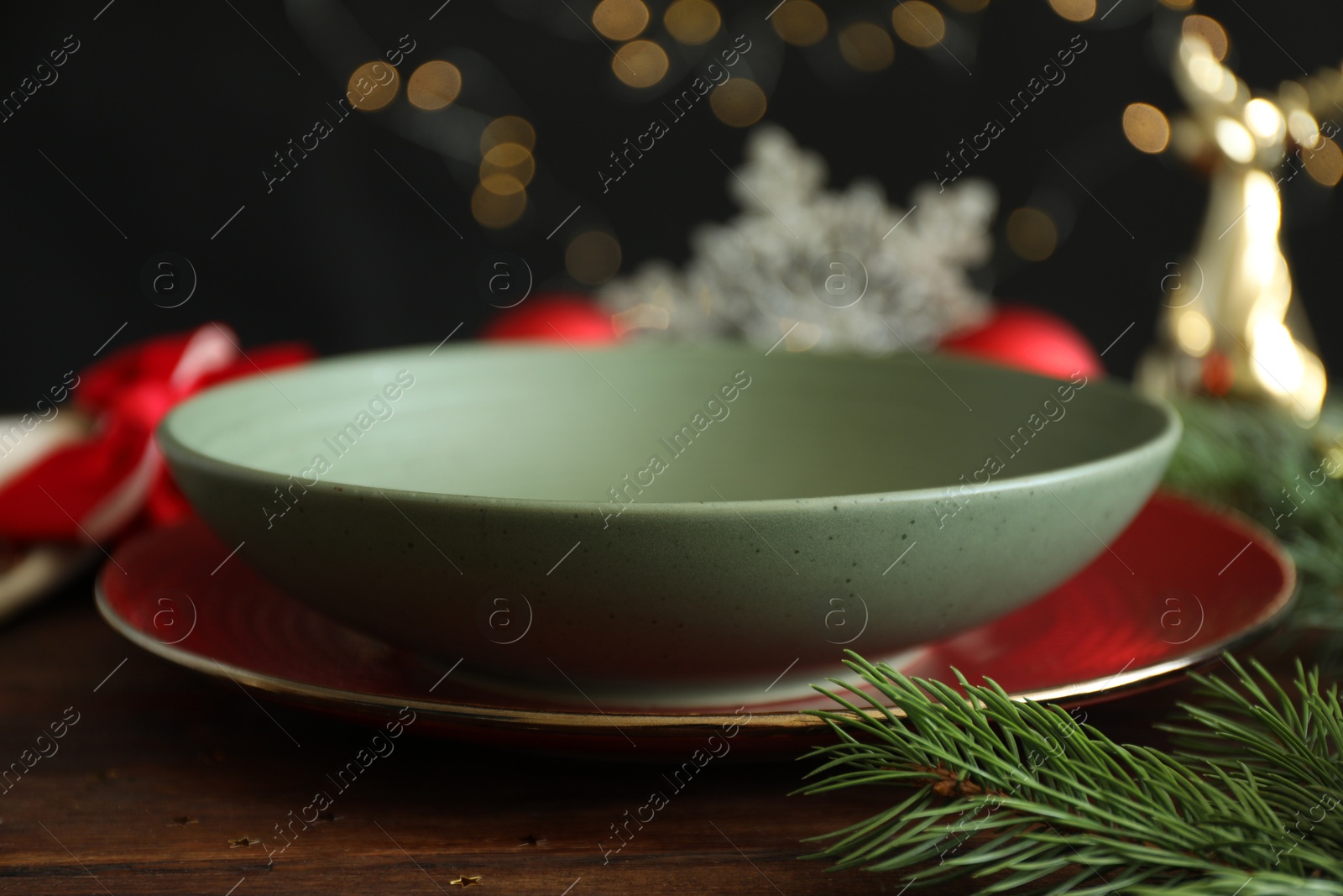 Photo of Christmas setting. Plate, bowl and fir branches on wooden table, closeup