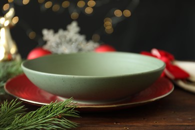 Photo of Christmas setting. Plate, bowl and fir branches on wooden table, closeup