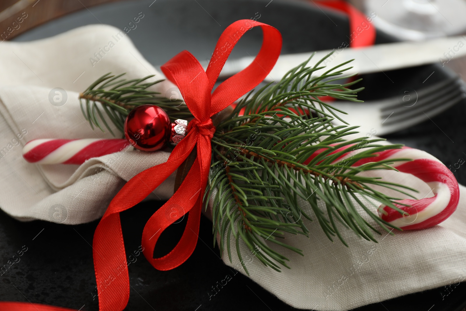 Photo of Christmas table setting. Napkin, fir branches, candy cane, bauble and ribbon on plate, closeup