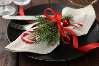 Photo of Christmas setting with plate, cutlery, fir branches and ribbon on wooden table, closeup