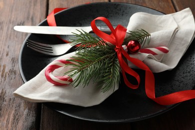 Photo of Christmas setting with plate, cutlery, fir branches and ribbon on wooden table, closeup