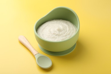 Photo of Delicious baby food in bowl and spoon on yellow background