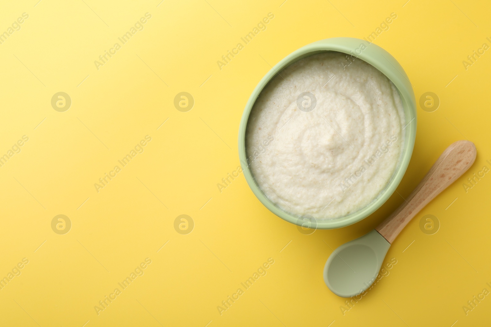 Photo of Delicious baby food in bowl and spoon on yellow background, top view. Space for text