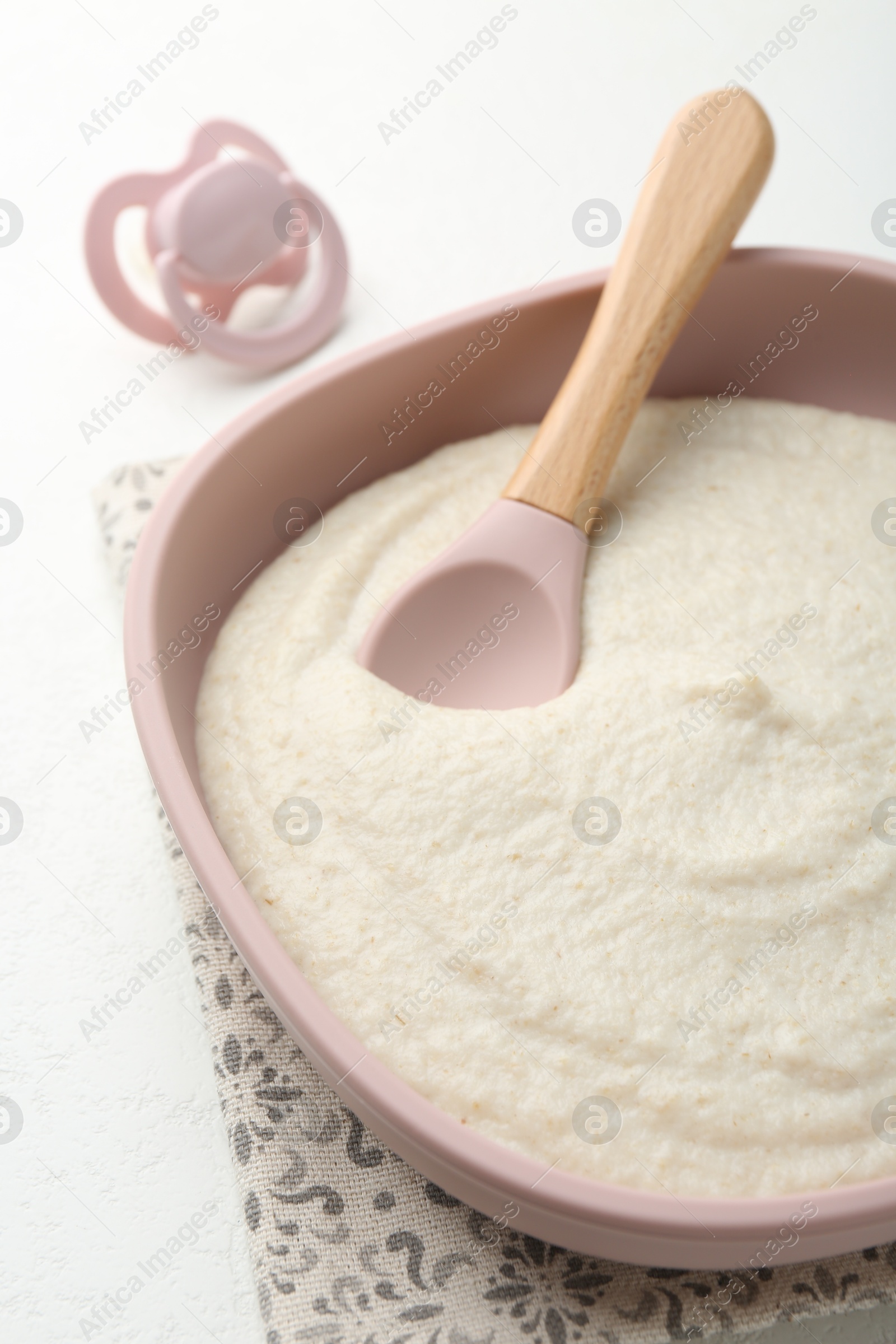 Photo of Delicious baby food in bowl with spoon and pacifier on white background, closeup