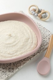 Photo of Delicious baby food in bowl with spoon and teether on white background, closeup