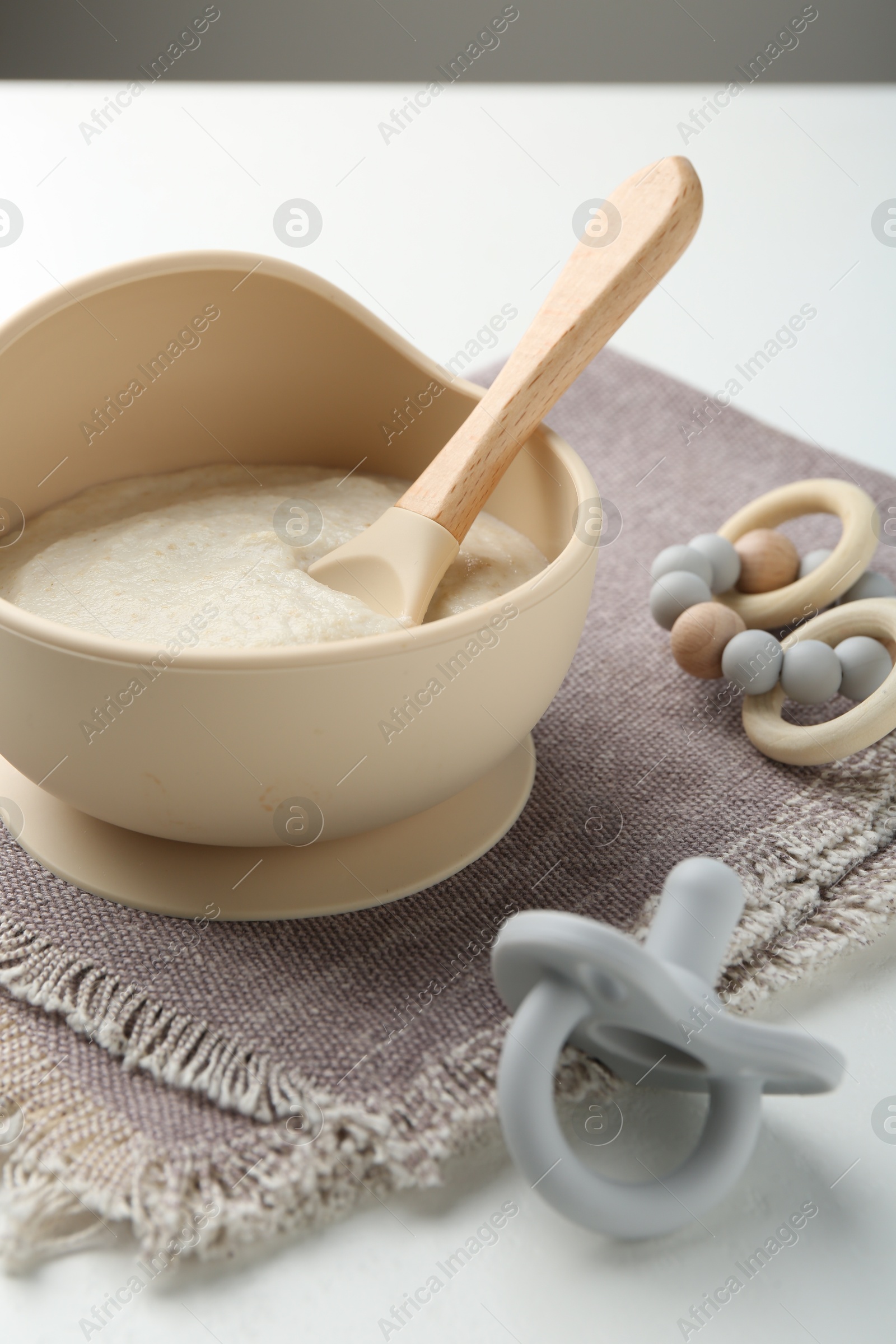 Photo of Delicious baby food in bowl with spoon, pacifier and teether on white background