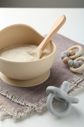 Photo of Delicious baby food in bowl with spoon, pacifier and teether on white background