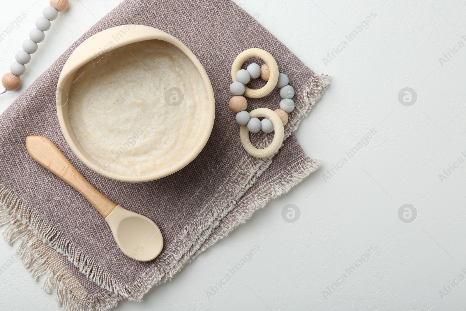 Photo of Delicious baby food in bowl with spoon and teether on white background, flat lay. Space for text