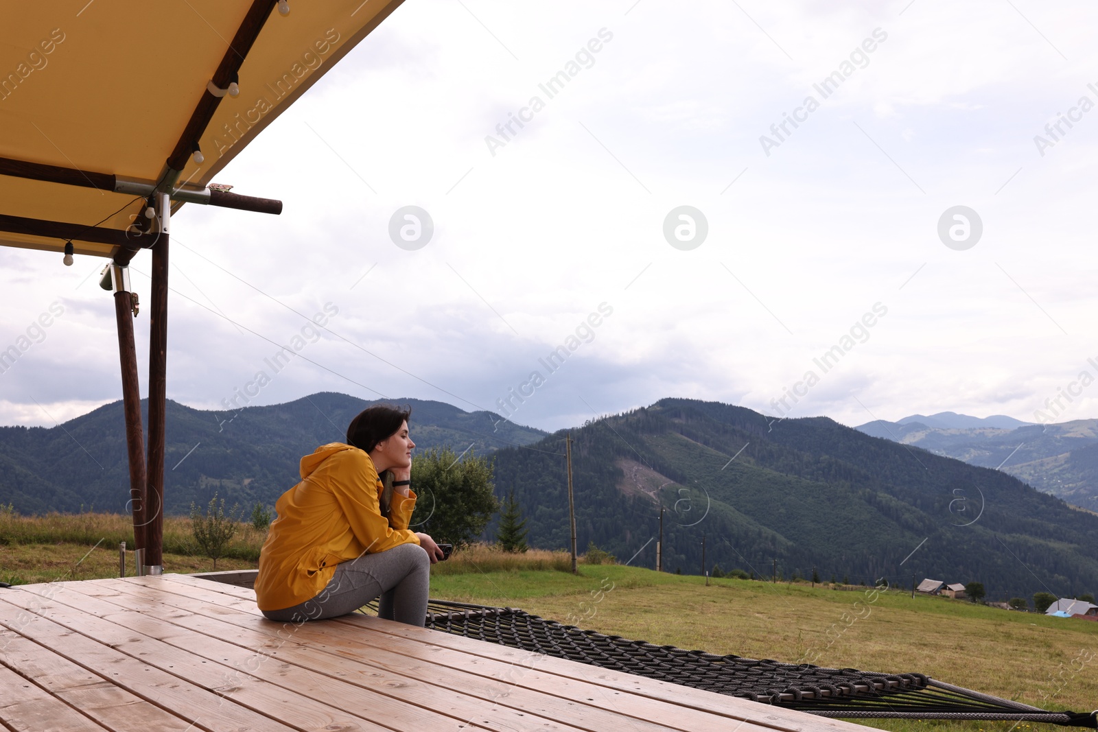 Photo of Young woman sitting on porch in mountains, space for text. Active tourism