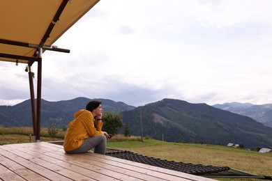 Young woman sitting on porch in mountains, space for text. Active tourism