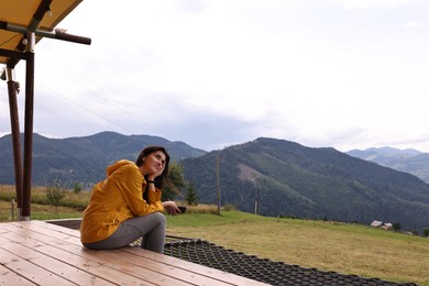 Photo of Young woman sitting on porch in mountains, space for text. Active tourism