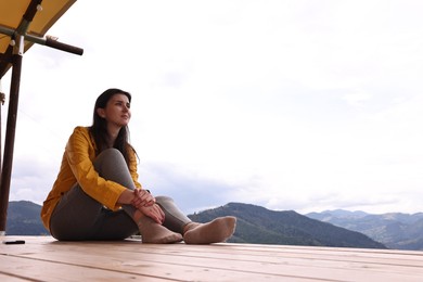 Photo of Young woman sitting on porch in mountains, space for text. Active tourism