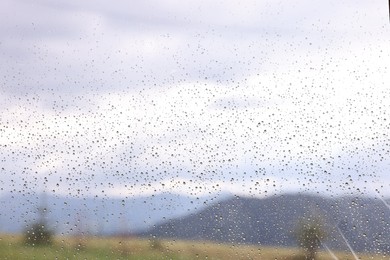 Photo of View of mountains through window with water droplets on rainy day, closeup