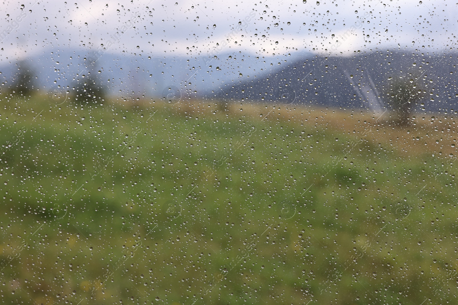 Photo of View of mountains through window with water droplets on rainy day, closeup