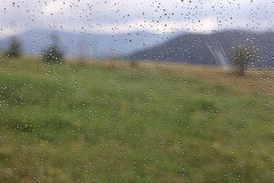 View of mountains through window with water droplets on rainy day, closeup