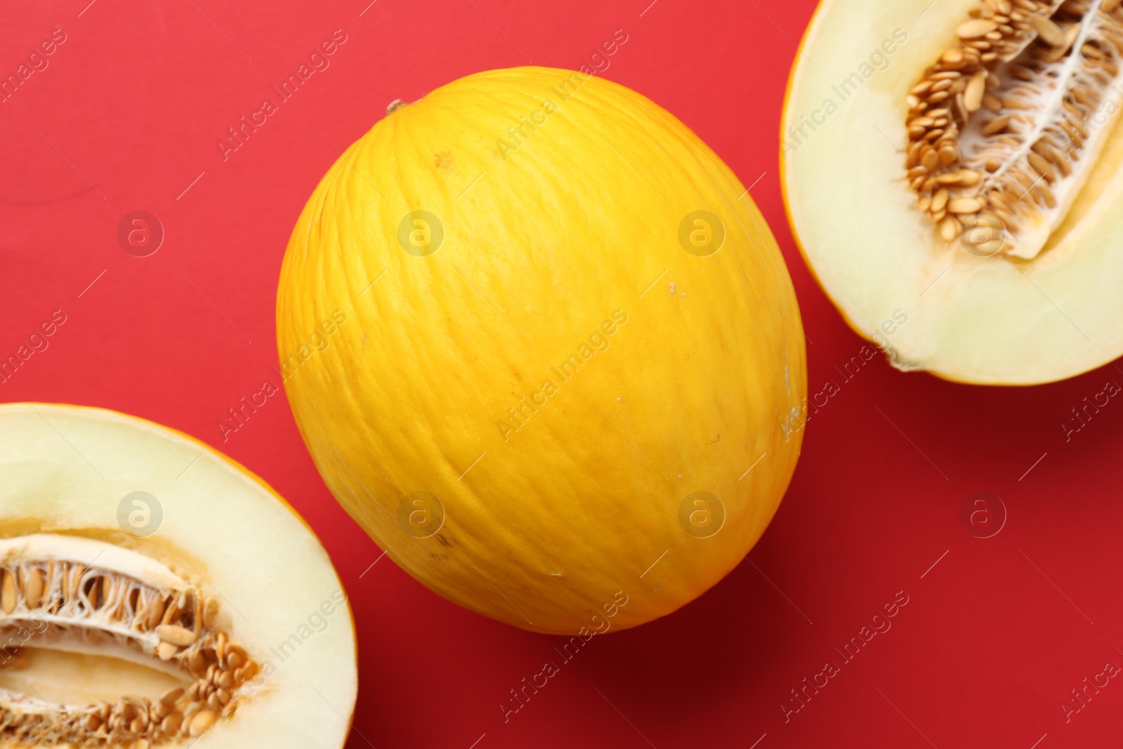 Photo of Whole and halves of fresh melon on red background, flat lay