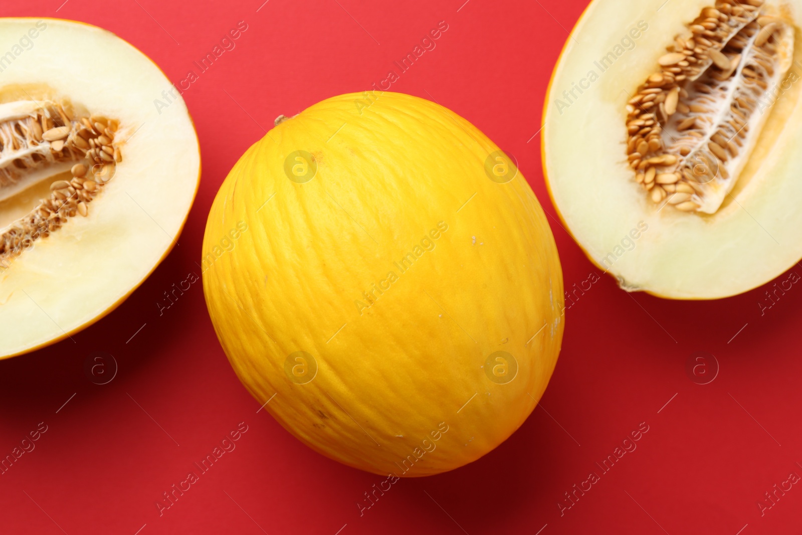 Photo of Whole and halves of fresh melon on red background, flat lay