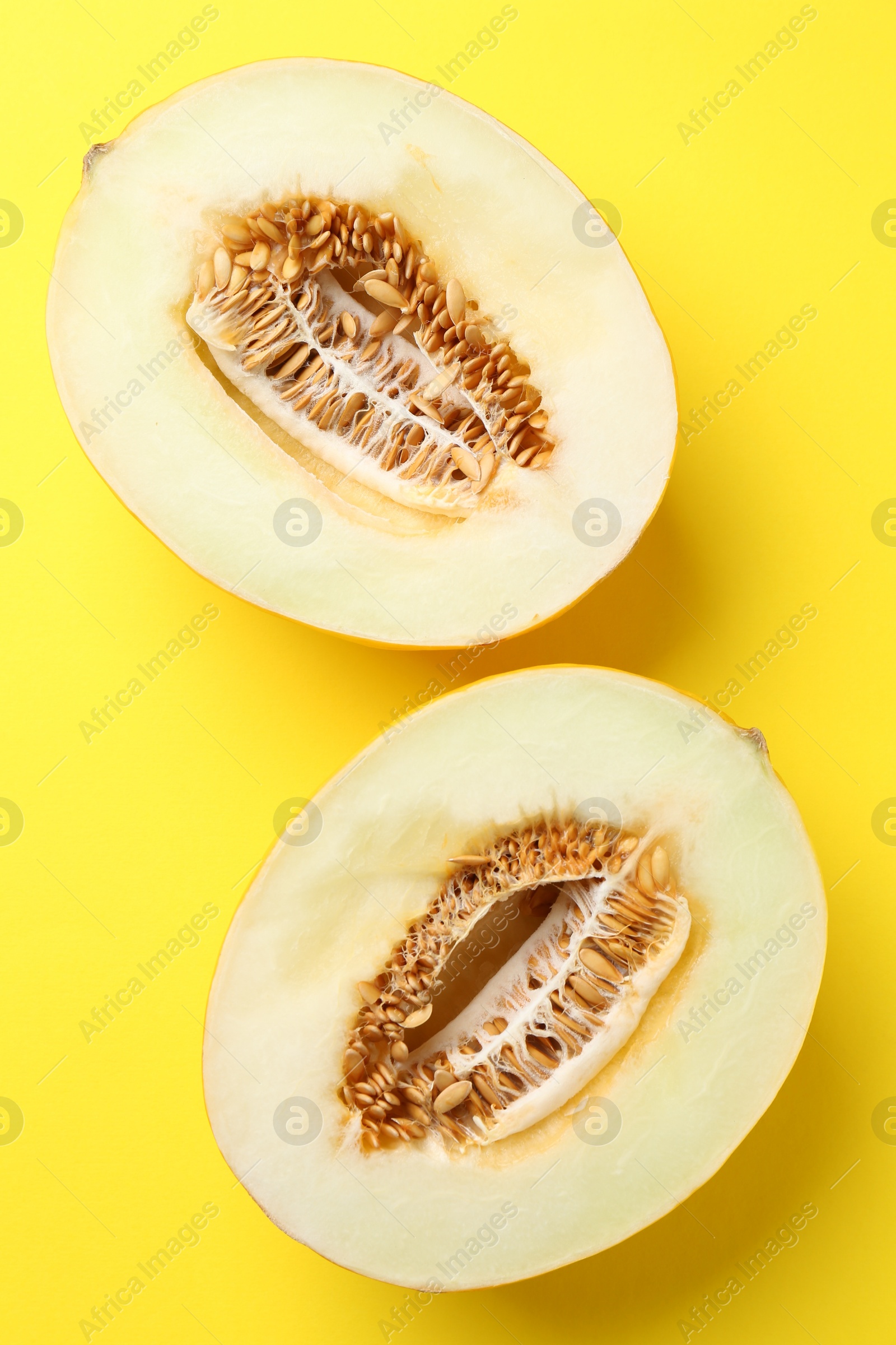 Photo of Halves of fresh melon on yellow background, top view